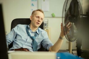 spocony mężczyzna przed wentylatorem w biurze
